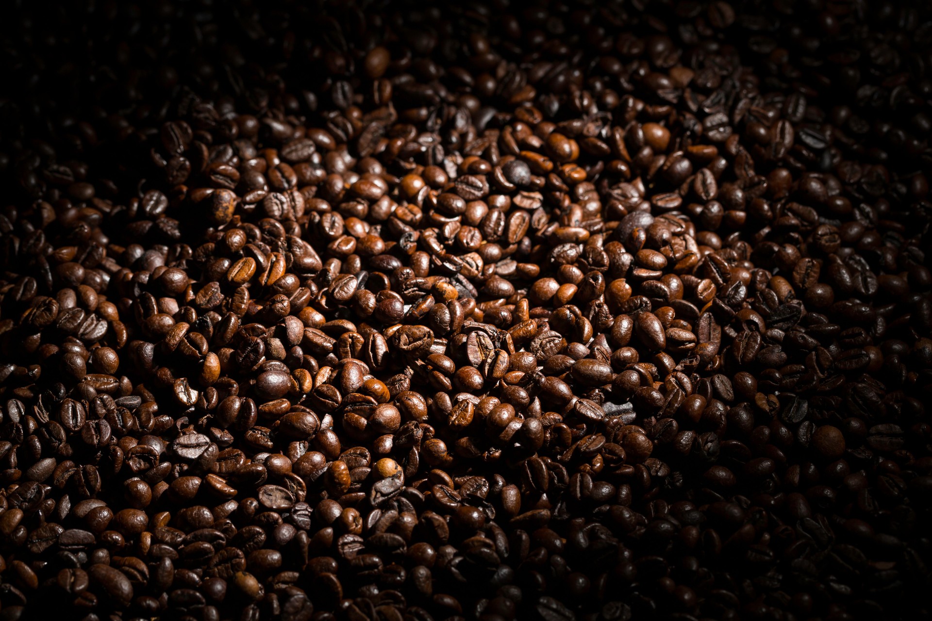 Grãos de café torrados ricos e escuros espalhados em uma superfície, criando uma textura e aroma convidativos em um ambiente mal iluminado